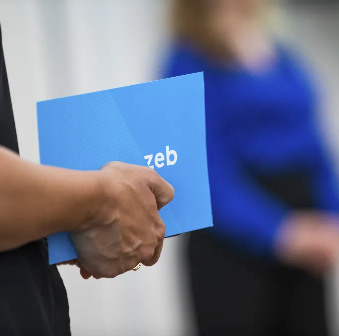 Eine Hand hält eine blaue Karte mit zeb-Logo. Eine Hand hält eine blaue Karte mit zeb-Logo.